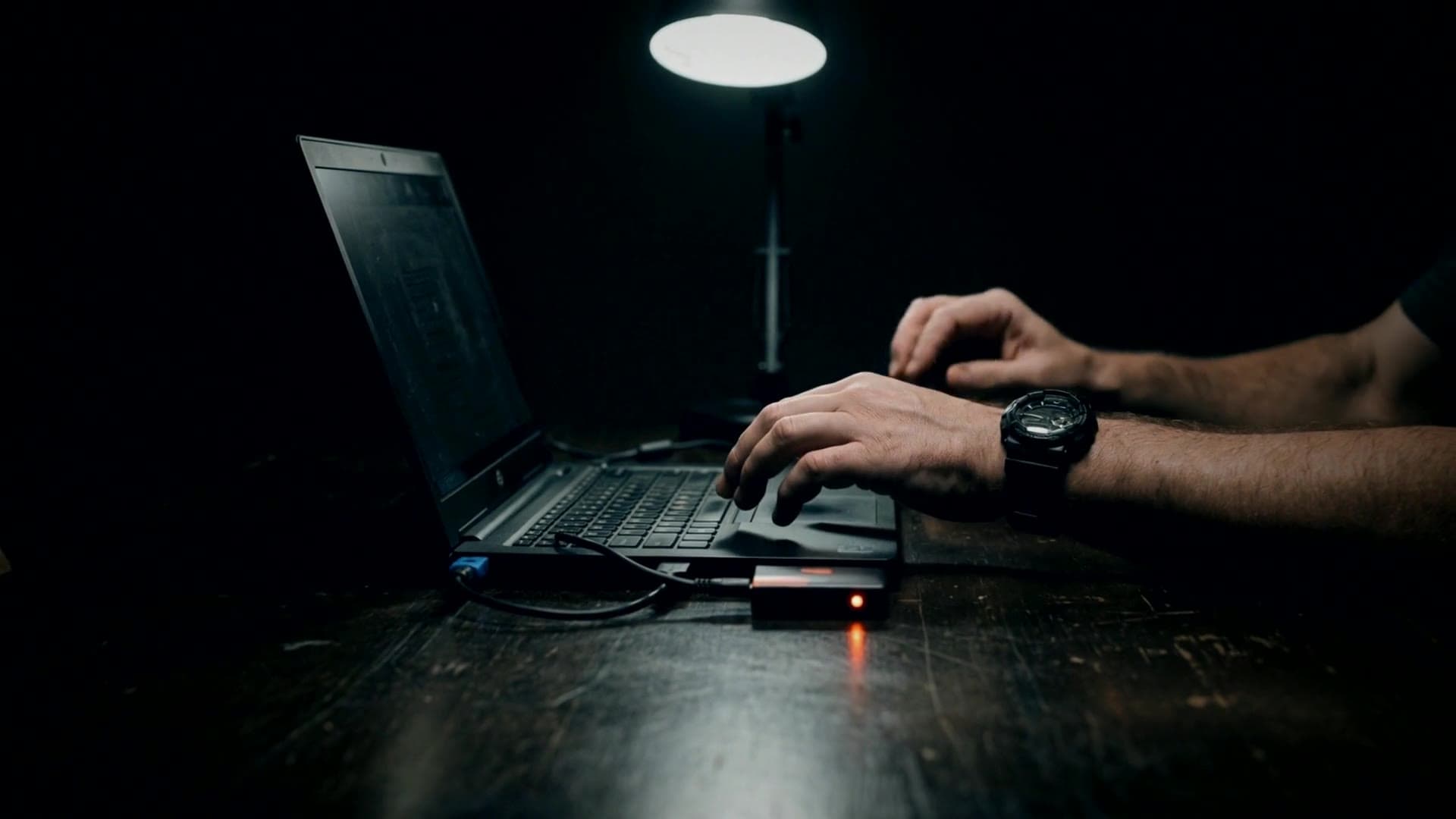 Two people working at one laptop late, a red status light on the desk